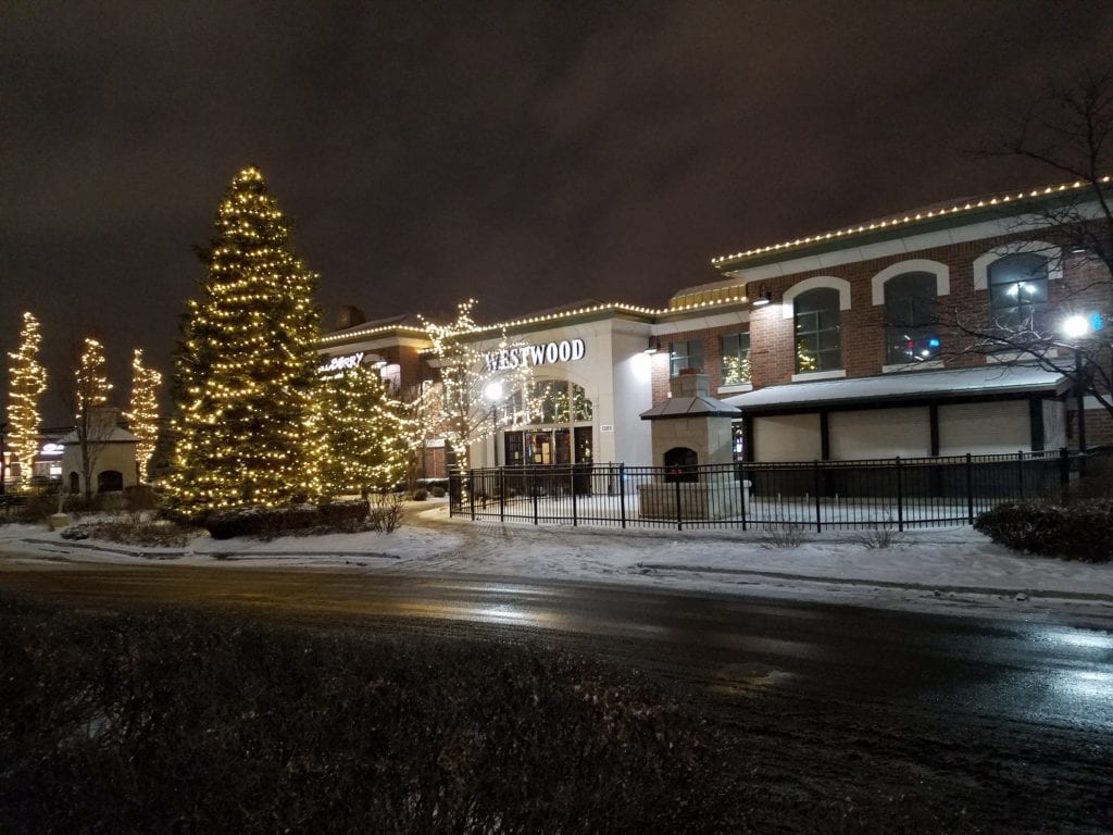 Restaurant with warm white roofline lights and tall evergreens covered in lights out front, snow on the ground