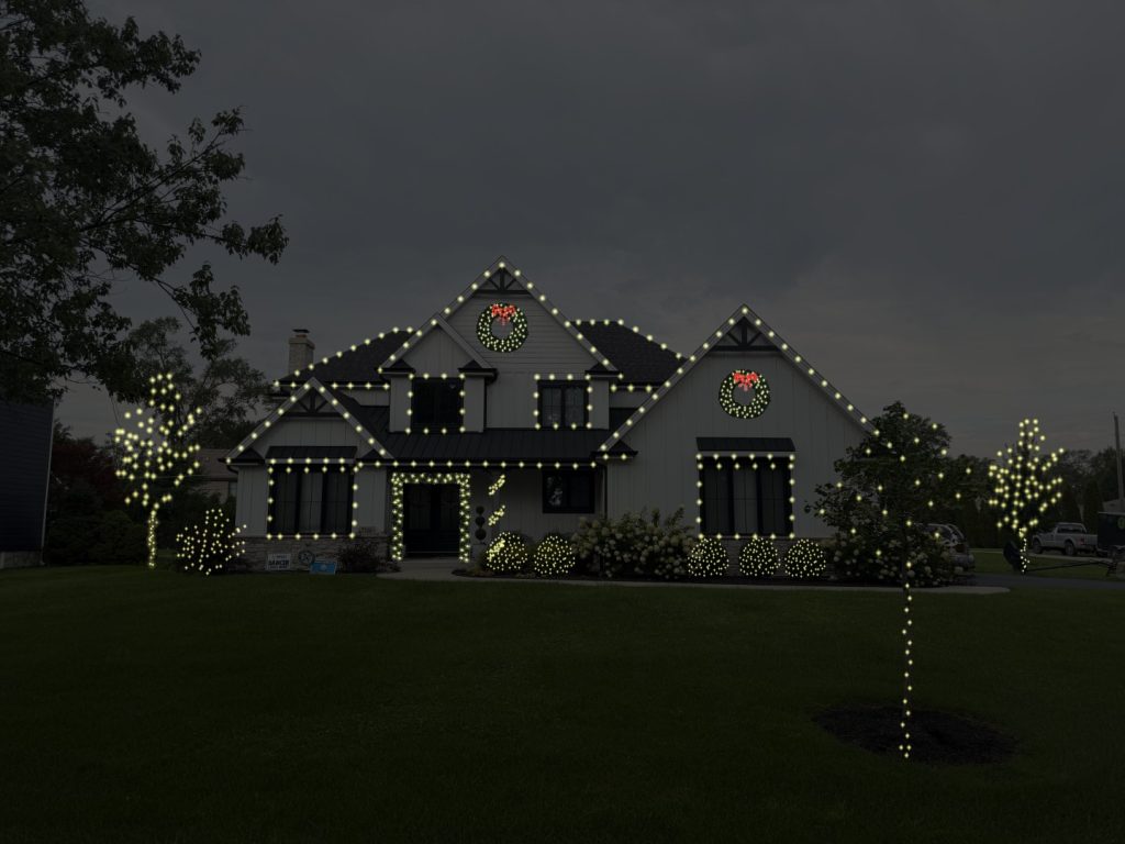 The same house with more of the roofline lit, the windows outlined, two wreaths and lit trees on both sides
