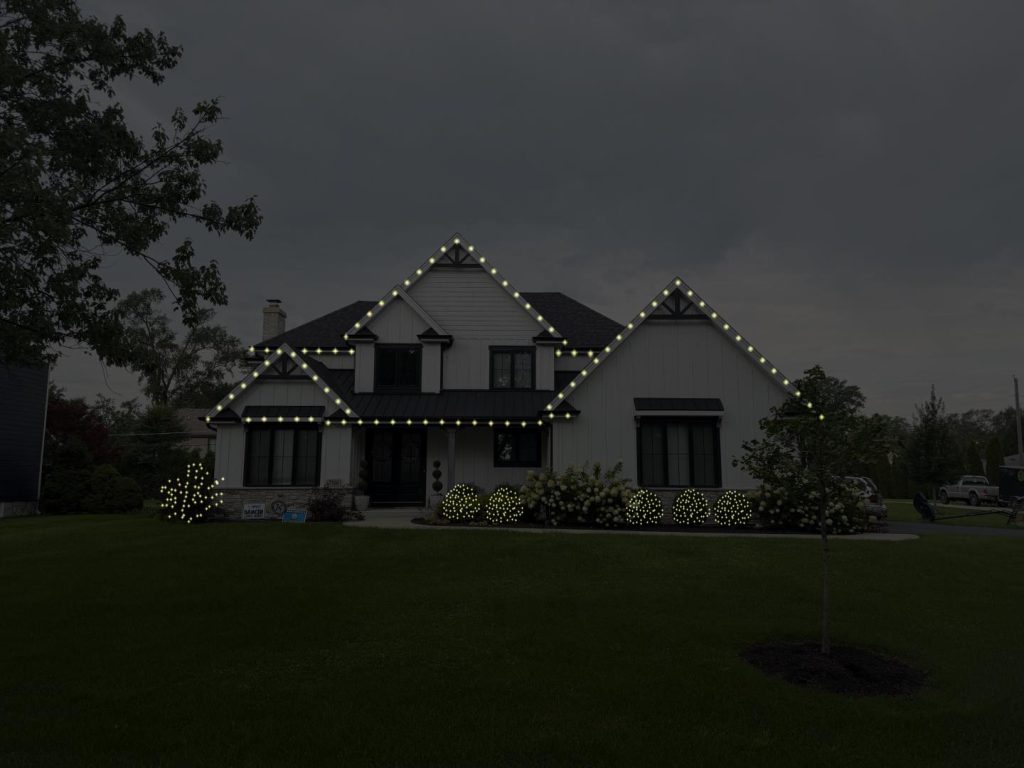 Design mockup of a two-story house at night with lights outlining the roofline peaks and lit shrubs along the front