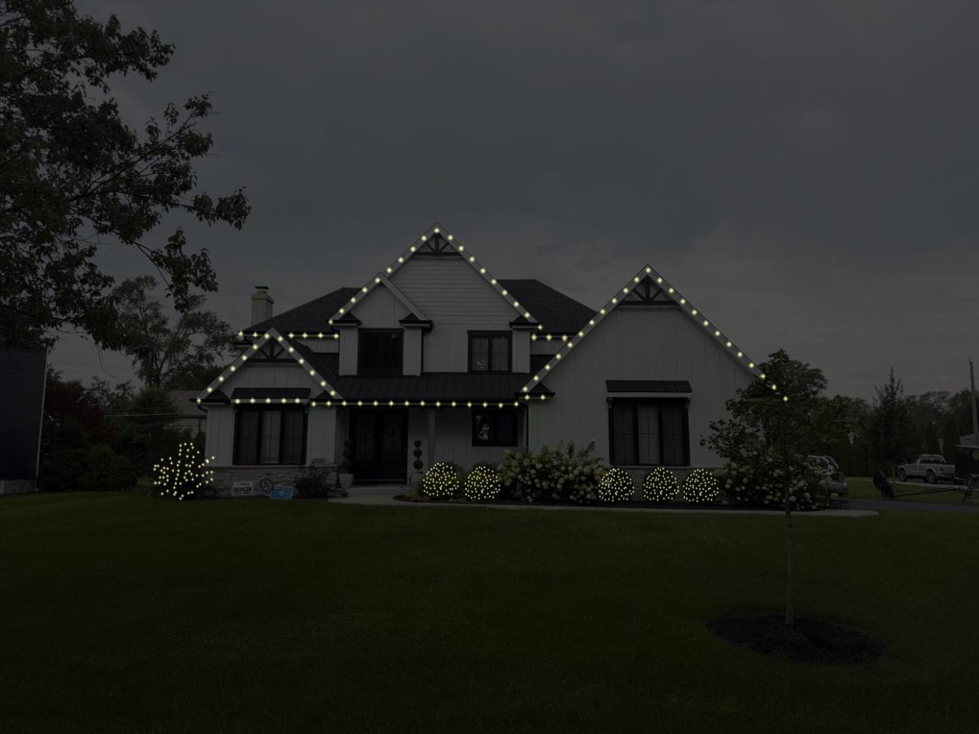 Signature package example: white house with the rooflines outlined in warm white lights and lit shrubs along the front